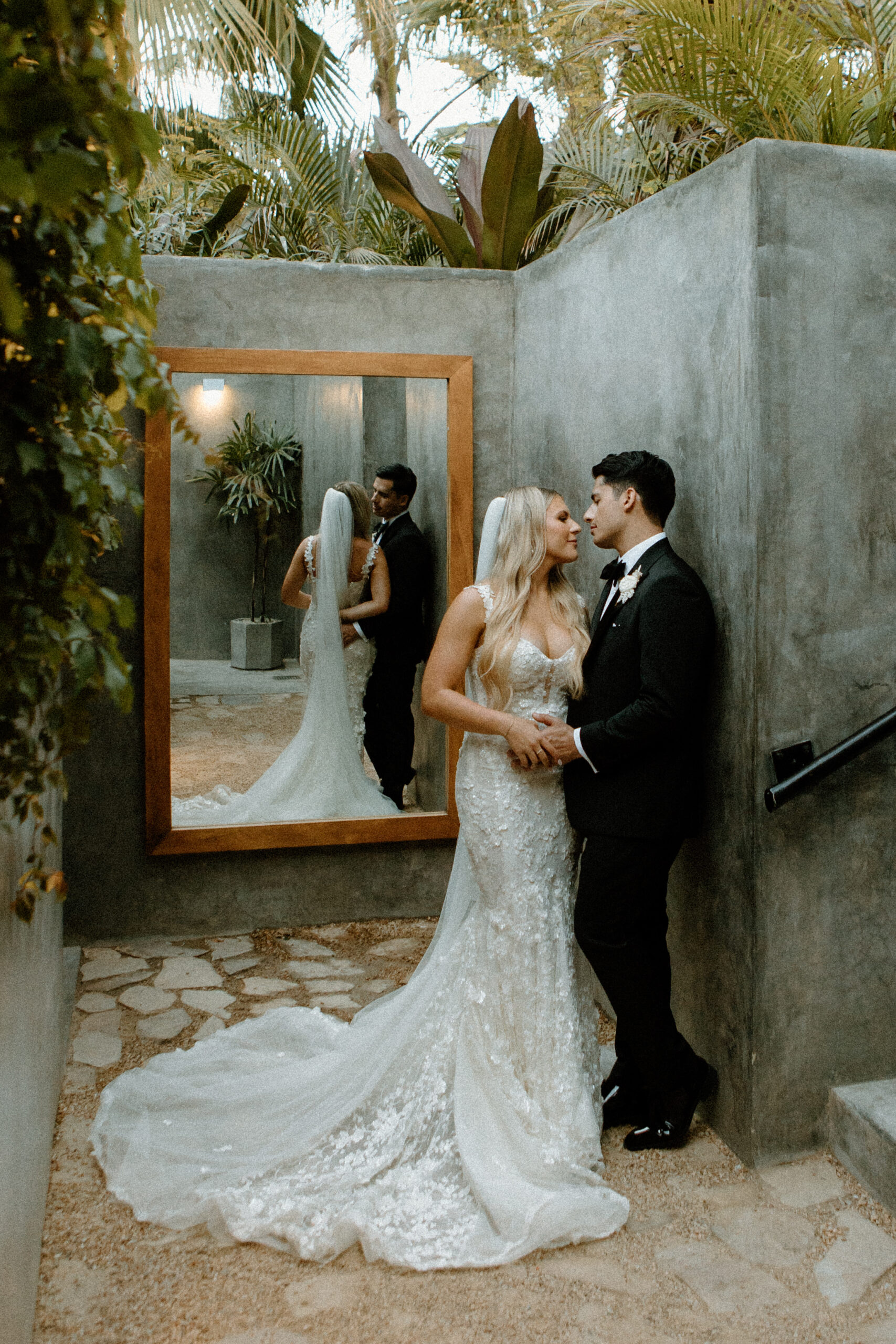 Acre Resort Wedding, couple standing married and holding hands at the bathroom area of Acre Resort with stone walls, a large mirror and lush jungle greenery
