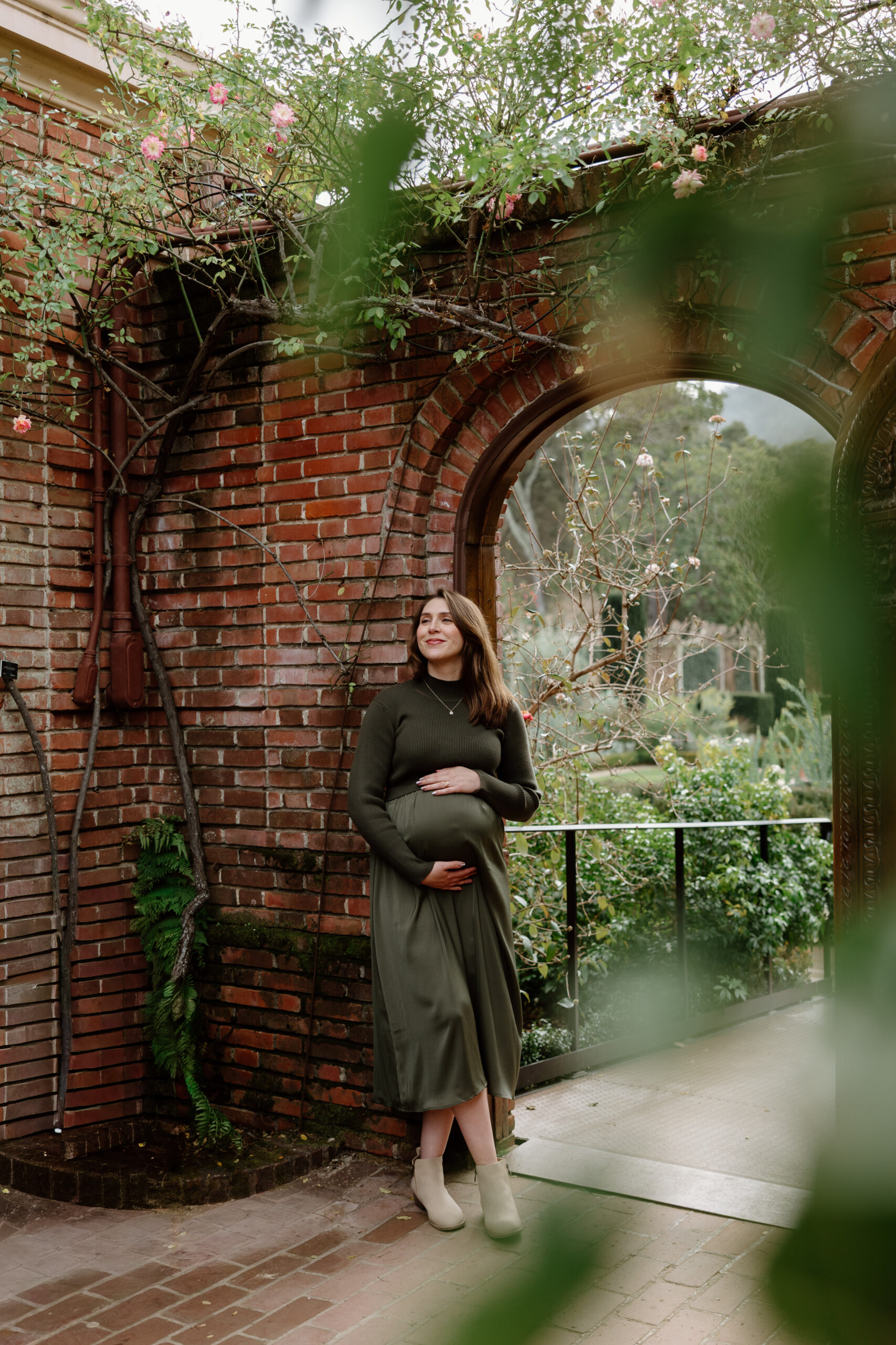 Filoli gardens maternity session, mom wearing a green dress up against a brick wall at Filoli gardens