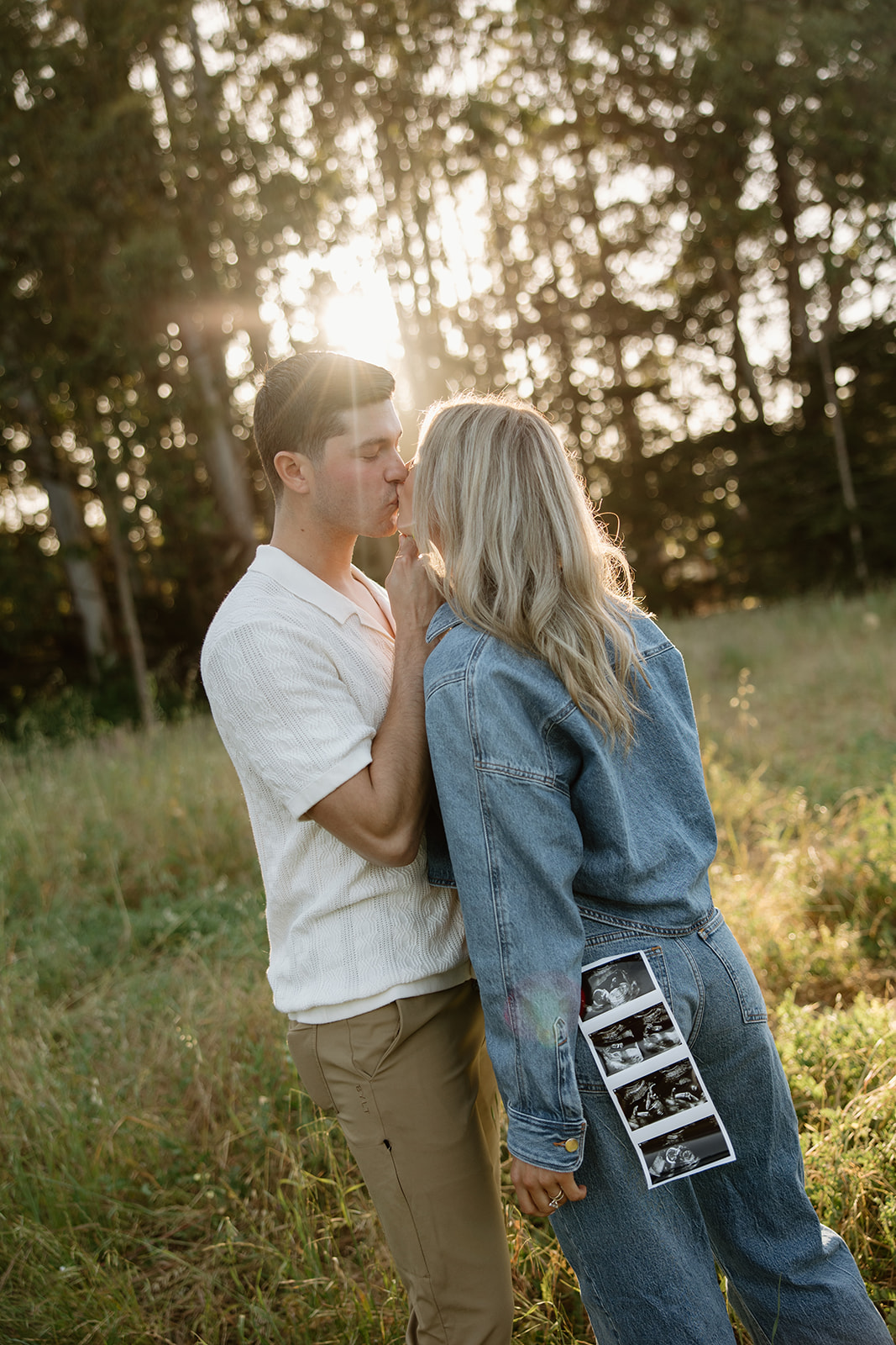 couple kissing during maternity photos in santa cruz california with ultrasound hanging out of back pocket of denim jeans